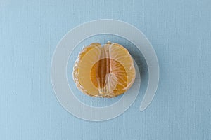 Half of a peeled tangerine on a pastel blue background.