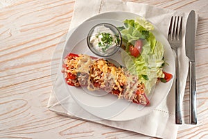 Half pointed bell pepper baked with rice  tuna  tomatoes and cheese on a white plate with lettuce salad and dip on white painted