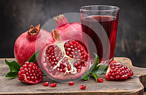 Half pomegranate and ripe pomegranate fruit with leaves near a pomegranate drink in a glass on a dark background