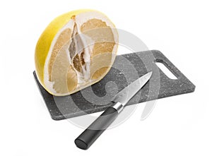 Half pomelo cut on the board. Knife.