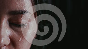 Half Portrait of a woman with closed eyes under rain on dark background. Feeling loneliness, drops flow down her face