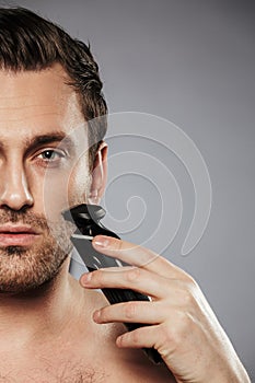 Half portrait of a young shirtless man shaving beard