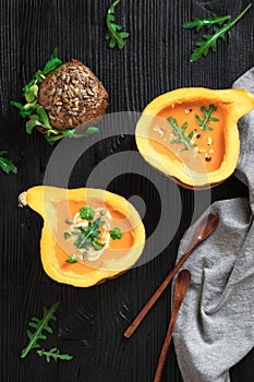 Half pumpkin with soup on black background. Flat lay. Vertical composition. Greens and veggies