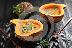 Half pumpkin with soup on black background. Horizontal composition. Greens and veggies