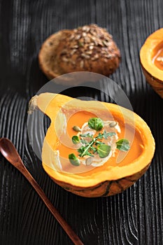 Half pumpkin with soup on black background. Vertical composition. Greens and veggies