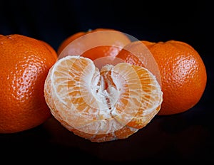 Half purified mandarine and whole tangerines. black background