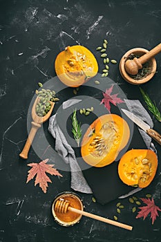 Half raw pumpkin with herbs, seeds and honey on a black stone background. Autumn food background. Thanksgiving and halloween