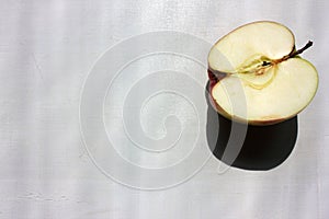 Half of the red apple on white wooden background. Hard light, deep shadow