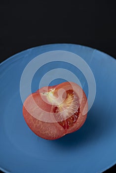 Half of red ripe juicy tomato on a blue plate on a black background Dark food photography