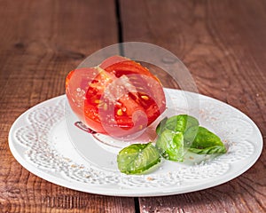 Half a red tomato and fresh basil leaves on a white plate