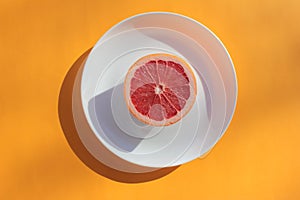 Half of ripe grapefruit on white plate on orange background. Flat lay food composition with bright citrus fruit