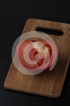 Half of ripe juicy tomato on a wooden board on a black background Dark food photography