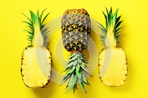 Half slice of fresh pineapple and whole fruit on yellow background. Top View. Copy Space. Bright pineapples pattern for