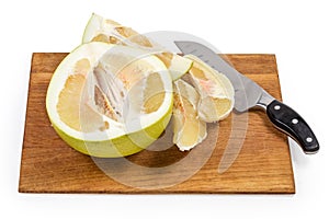 Half and slices of ripe pomelo, knife on cutting board