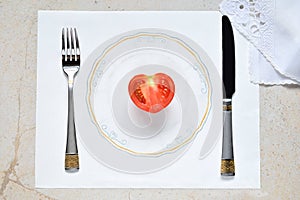 Half a tomato in the form of a heart on a painted plate. Concept of vegetarian food. Restrictions on food. Small portion of food o