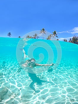 HALF UNDERWATER: Woman snorkels towards the camera and makes the ok gesture.