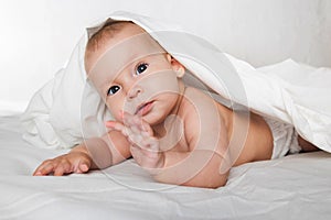 A half-year-old cute baby in a diaper and a towel lies on his stomach and looks cheerfully at the camera