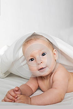 A half-year-old cute baby in a diaper and a towel lies on his stomach and looks cheerfully at the camera,,