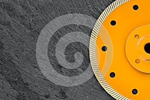 Half of a yellow diamond cutting wheel with a threaded nut on a dark gray granite background, the concept of stone processing in