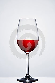 Halffull wine pure wine glass with red wine against light background with reflection.