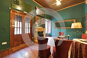 Hall of a vintage-style bar with green walls, a marble fireplace and armchairs upholstered in red fabric