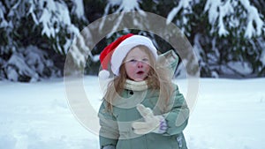 Hallo Christmas little girl in red santa claus hat. New Year's child in the forest with snow. Winter park and trees in