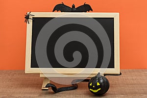 Halloween background concept. Front view of blackboard with decoration objects, pumpkin, bats, snake, spiders on orange backdrop