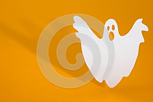 Halloween background concept. Funny ghost doing boo gesture and graphic shade behind on orange table