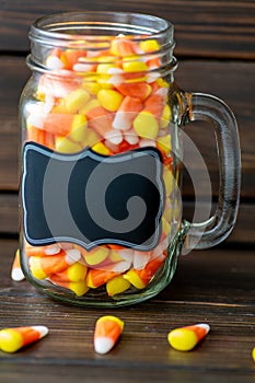 Halloween background frame consisting of a jar full of candy corn on a dark wooden table with a black table that you can personali