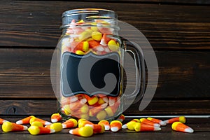 Halloween background frame consisting of a jar full of candy corn on a dark wooden table with a black table that you can personali