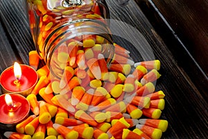 Halloween background frame consisting of a jar full of candy corn on a dark wooden table with a black table that you can personali