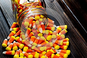 Halloween background frame consisting of a jar full of candy corn on a dark wooden table with a black table that you can personali