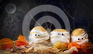 Halloween background. Spooky potatoes wrapped in medical bandages in autumn leaves on a dark night. Halloween food. Copy space photo