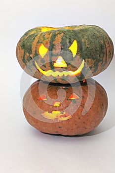Halloween big green striped pumpkin on smaller orange pumpkin. jack o`lantern, carved face on empty pumpkin. light of candle