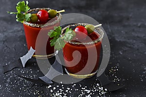 Halloween Bloody Mary cocktails served with pickled veggies tomatos, olive and celery and paper bats on a dark background. Close