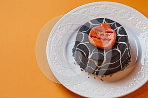 Halloween cake in a white plate. Surface orange background.