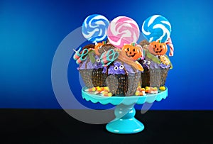 Halloween candyland drip cake style cupcakes with candy on blue background.