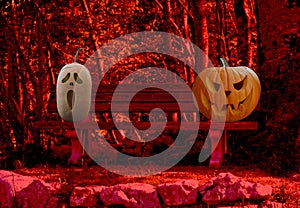 Halloween celebration two scary and spooky carved pumpkins on a park bench in a horror forest landscape