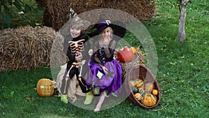 Halloween children in black and orange Halloween costume and hat play with pumpkin in garden or backyard. Kids trick or