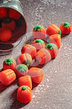 Halloween-colored pumpkin-shaped candy canes are placed on a gray table with sunlight in the background