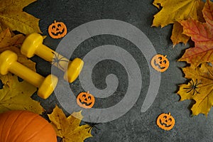 Halloween composition with gym dumbbells, decorations and autumn pumpkin on fall leaves.