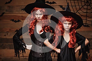 Halloween Concept - Beautiful caucasian mother and her daughter with long red hair in witch costumes with angry fussy facial expre