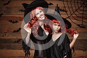 Halloween Concept - Beautiful caucasian mother and her daughter with long red hair in witch costumes celebrating Halloween posing