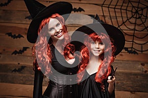 Halloween Concept - Beautiful caucasian mother and her daughter with long red hair in witch costumes and magic wand celebrating Ha