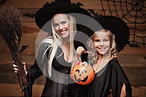 Halloween Concept - beautiful caucasian mother and her daughter in witch costumes celebrating Halloween with sharing Halloween can