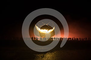 Halloween concept. Blurred silhouette of giant Jack-o-lantern pumpkin with scary smiling face behind crowd at night. People looks