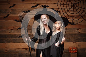 Halloween Concept - cheerful mother and her daughter in witch costumes celebrating Halloween posing with curved pumpkins over bats