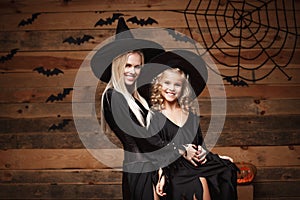 Halloween Concept - cheerful mother and her daughter in witch costumes celebrating Halloween posing with curved pumpkins over bats