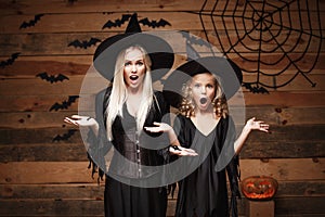 Halloween Concept - cheerful mother and her daughter in witch costumes shocking with something.