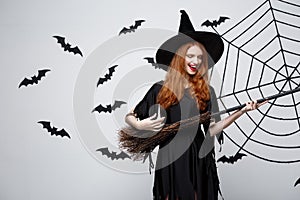 Halloween Concept - Happy elegant witch enjoy playing with broomstick halloween party over grey background.